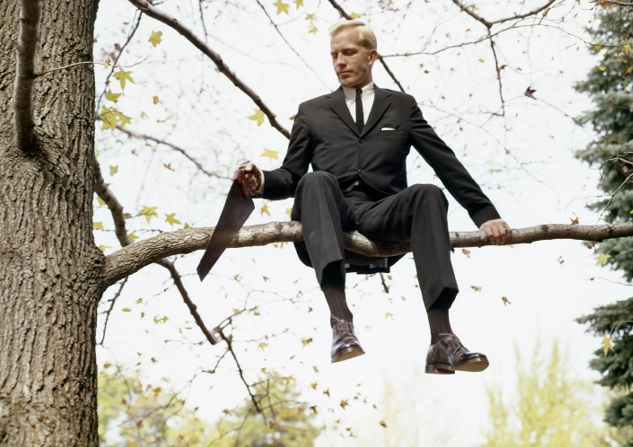 Suit man sitting sawing branch